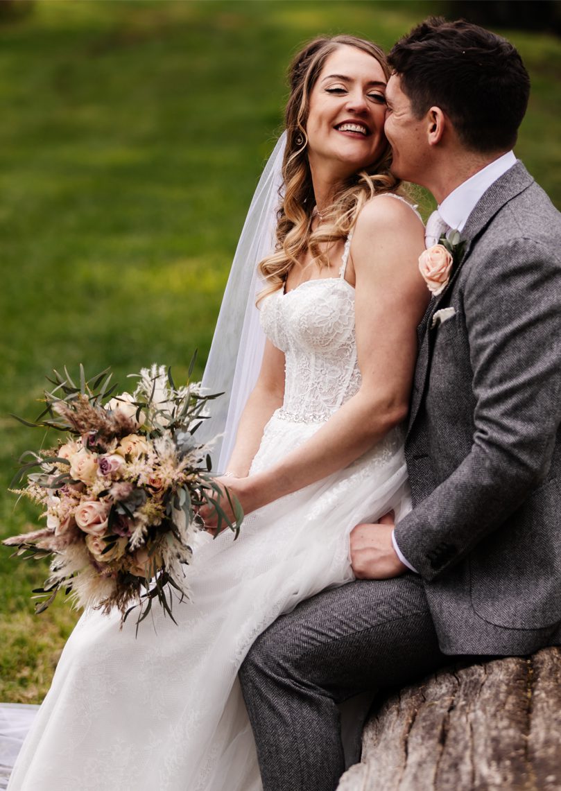 Bride and groom cuddling sitting on a log