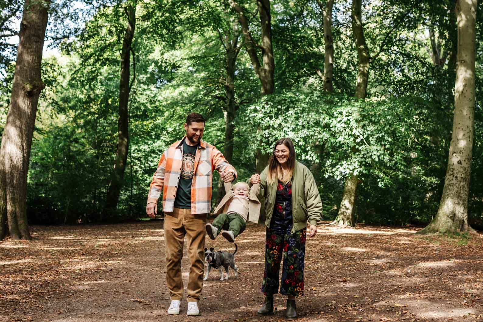 Parents swinging their son while family dog watches during a Birmingham photoshoot”