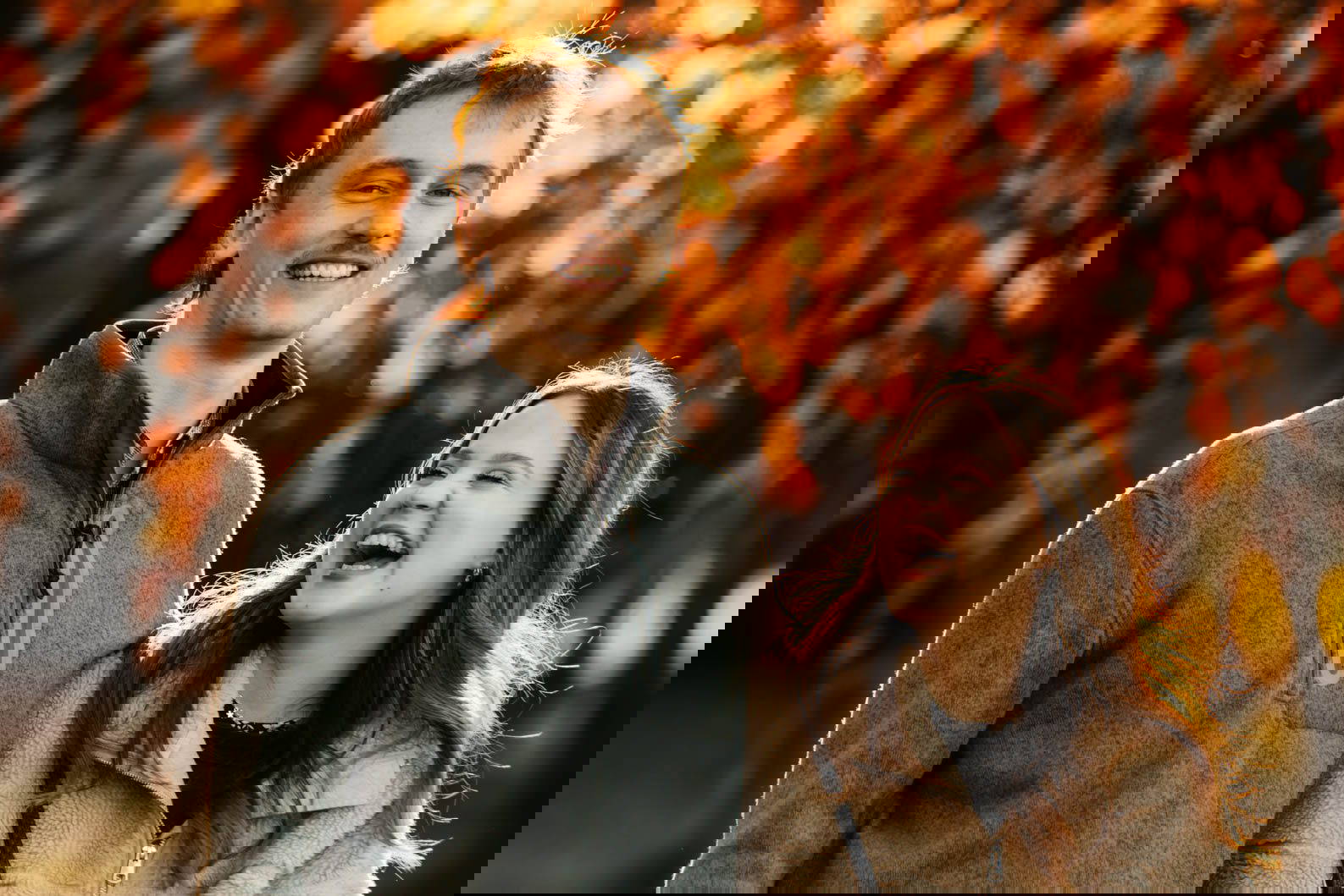 Laughing engaged couple surrounded by autumn leaves at Cannon Hill Park in Birmingham during their pre-wedding shoot.