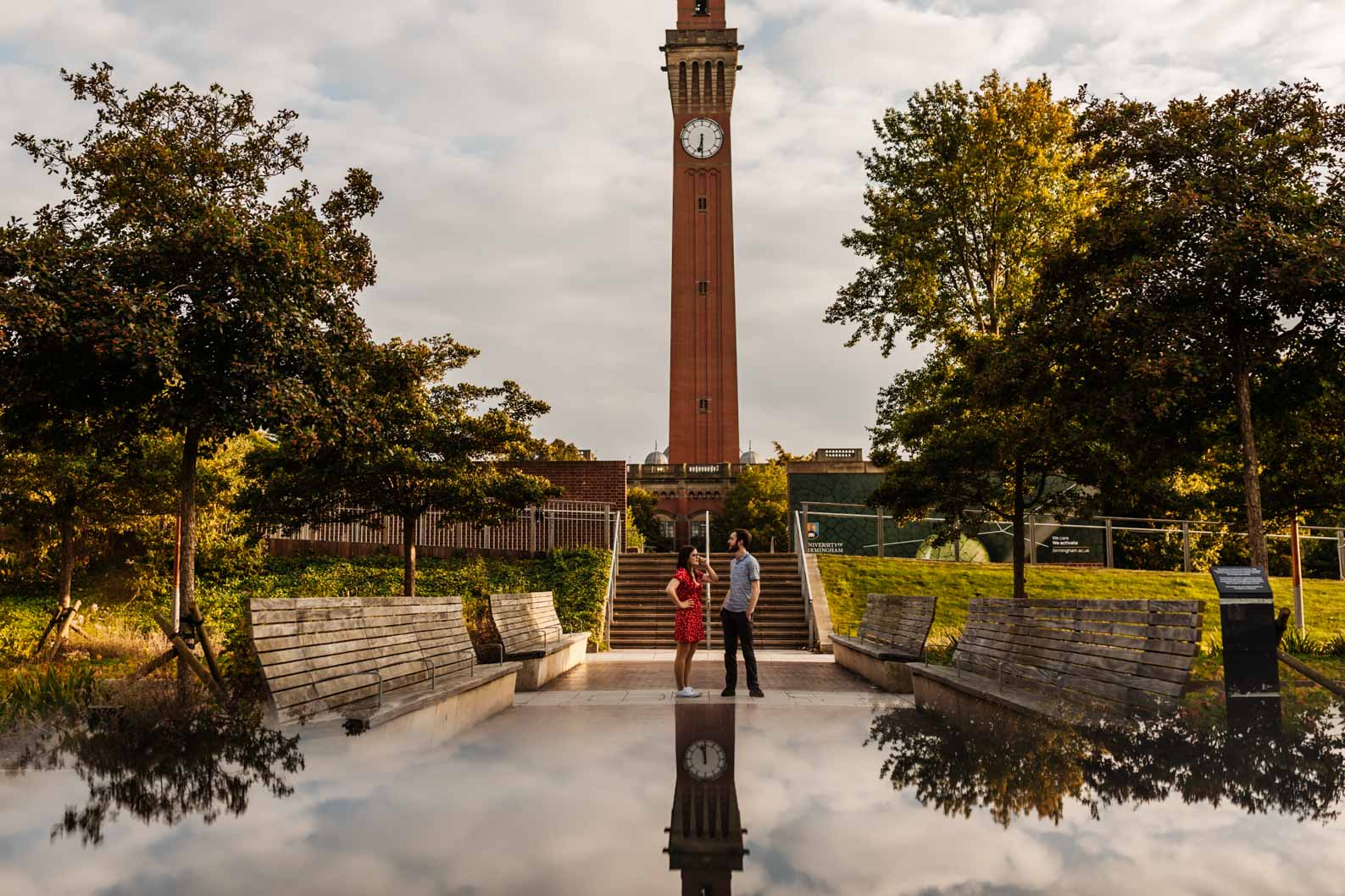 Couple standing beneath the clock tower at University of Birmingham Edgbaston during engagement shoot.