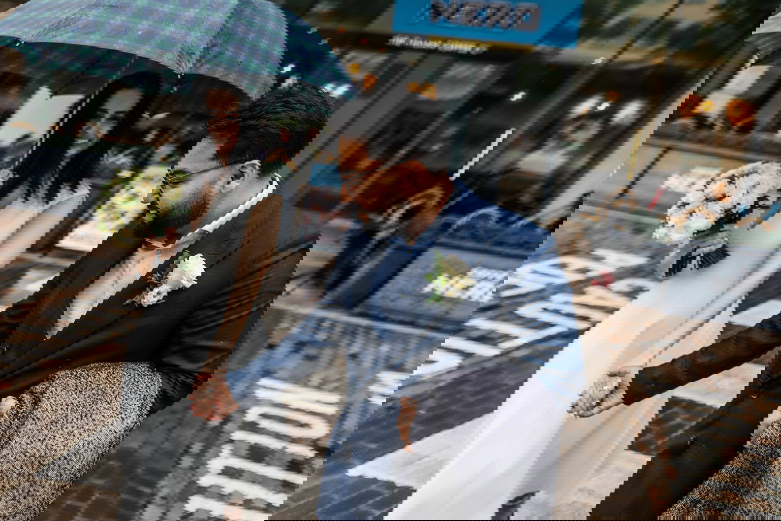 Bride and groom smiling while crossing a road together under an umbrella during a rainy Birmingham wedding