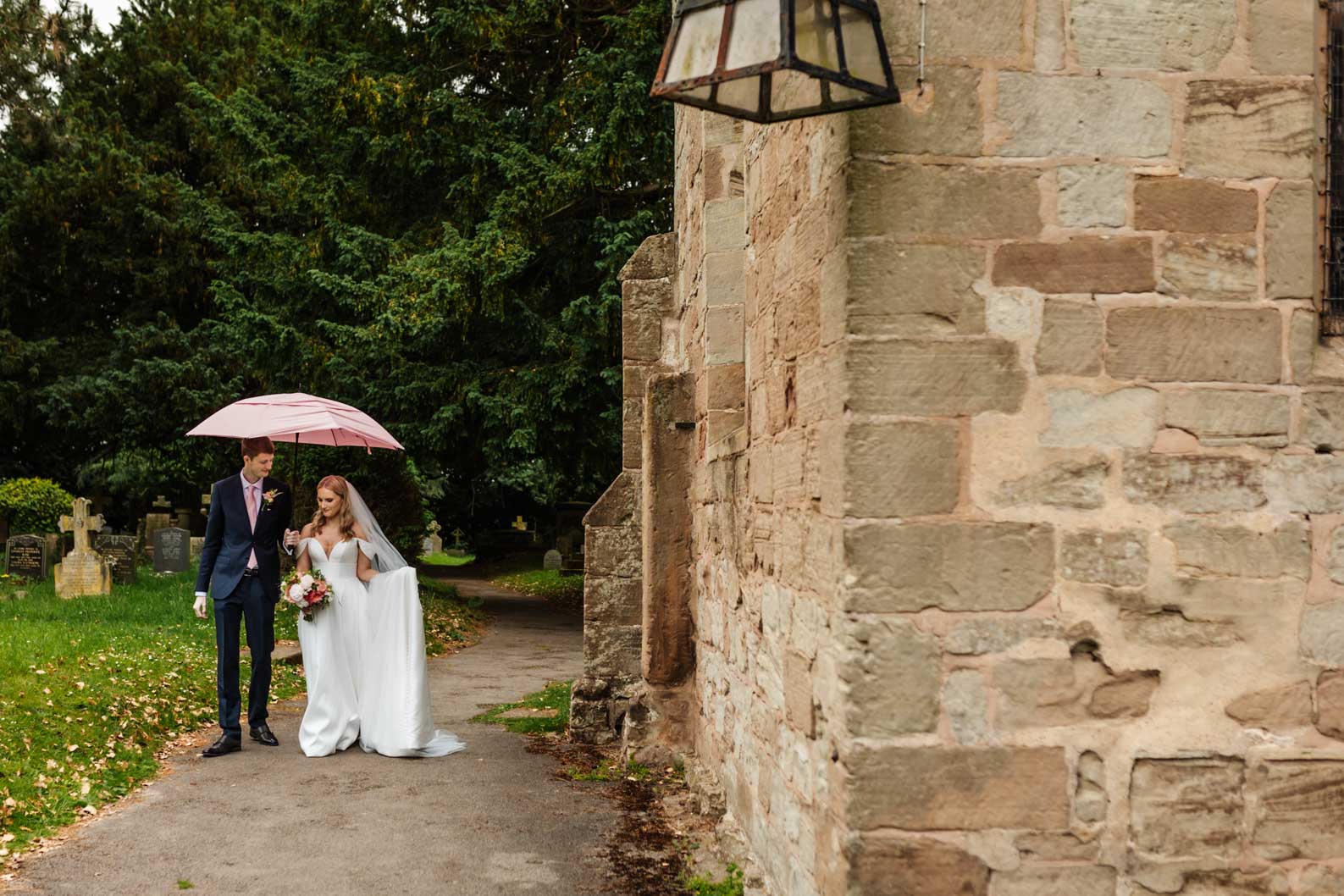 Bride and groom smiling at each other under a pink umbrella during a rainy wedding in Worcestershire