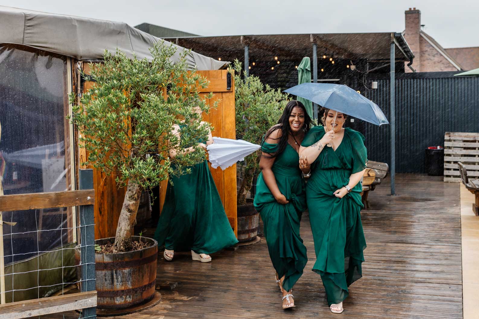 ridesmaids laughing and smiling together under heavy rain at a Warwickshire Wedding, embracing the rainy wedding day