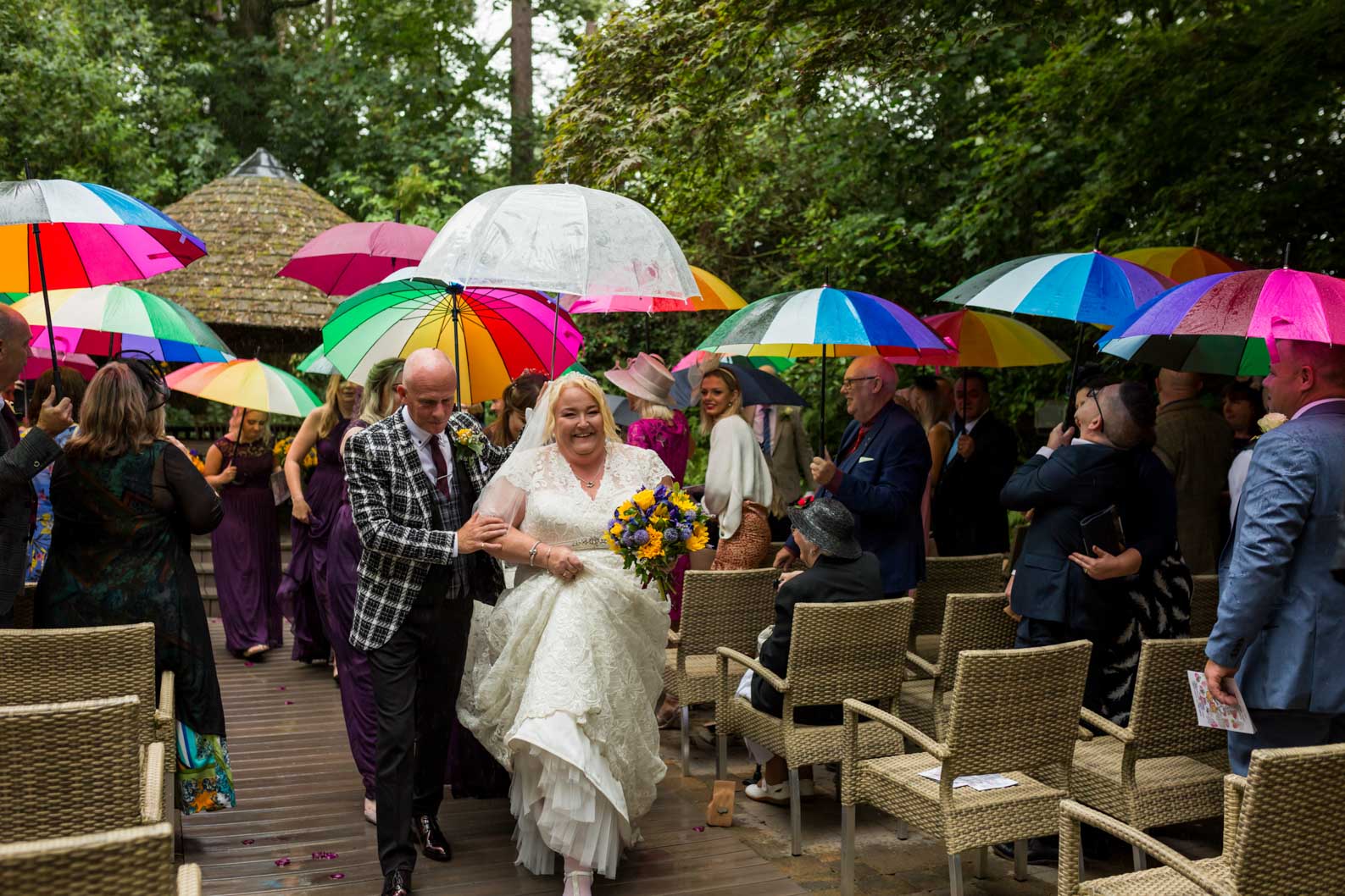 Newly married couple walking down the aisle under colourful umbrellas at Moxhull Hall on a rainy West Midlands wedding day