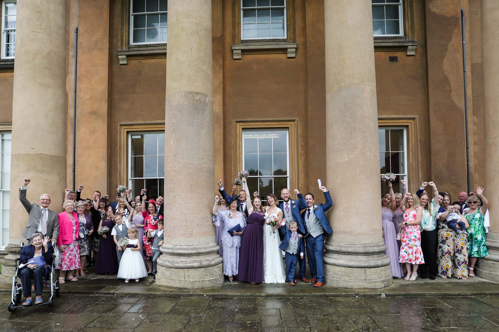 Wedding party posing together under covered columns at Himley Hall during a rainy West Midlands wedding