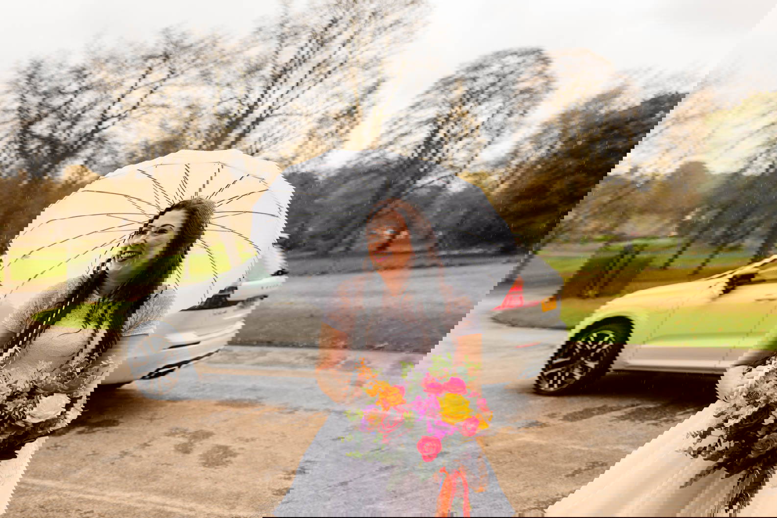 Bride with a big smile holding a white umbrella outside Dudley Register Office before her wedding ceremony, embracing the rainy day